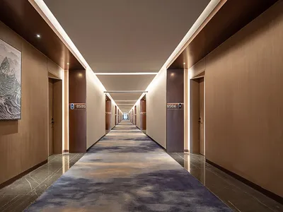 Long modern luxury hotel corridor with warm wood panel walls, dark marble flooring, patterned blue and beige carpet runner, recessed ceiling lighting, and large abstract mountain artwork on the left wall.