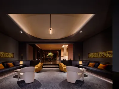 Modern luxury hotel lobby with white curved lounge chairs, golden yellow armchairs, navy blue velvet banquettes with orange pillows, dramatic cove lighting and geometric gold wall accents.