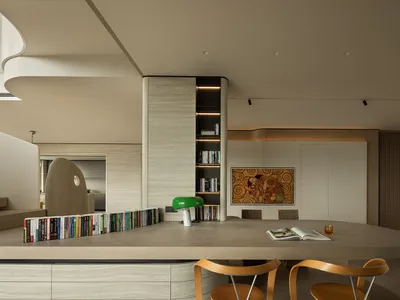 Modern dining area featuring a large curved oak counter, wooden chairs, built-in bookshelf with LED lighting, and a Gustav Klimt painting on the wall.