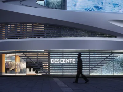 Night view of the modern curved facade of Descente store in Taipei with large digital ocean wave display and a pedestrian walking by.