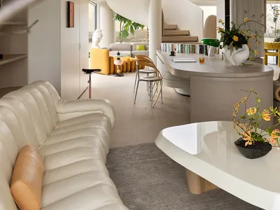 Modern open-concept living room featuring a cream ribbed leather sofa, curved wooden kitchen island, dramatic white spiral staircase, and vibrant yellow furniture in the background.