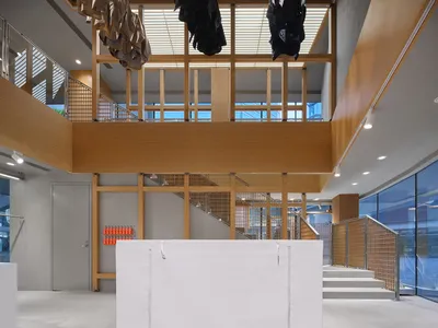 Modern double-height retail interior with light oak wood structural beams, white walls, concrete floor, and clothing hanging from the ceiling.