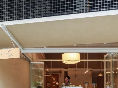 男子坐在咖啡店外的水磨石階梯上享用咖啡，吧台師傅正在店內準備飲料。