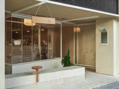 現代極簡風格咖啡店外觀，混凝土立面、大片玻璃窗、木製招牌與懸掛吊燈。
