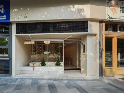現代極簡咖啡廳店面，展現裸露混凝土、大面積玻璃窗、內嵌混凝土花台種植常綠小樹，以及木質吊燈。