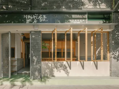 汕尾擂茶飯店街景，現代店面結合淺色木櫃、灰色混凝土柱、綠色基座與可開合的大型木窗，上方為深綠色招牌。