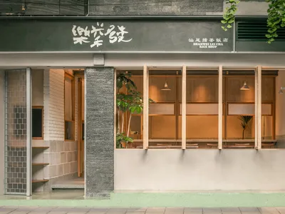 汕尾擂茶飯店街景，深綠色招牌、清水模紋理柱體、淺木色窗框與溫暖室內照明。