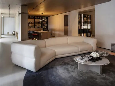 Modern double-height living room featuring a large white bouclé sectional sofa, dark walnut wood paneling with integrated lighting, marble coffee table, and dark grey area rug.