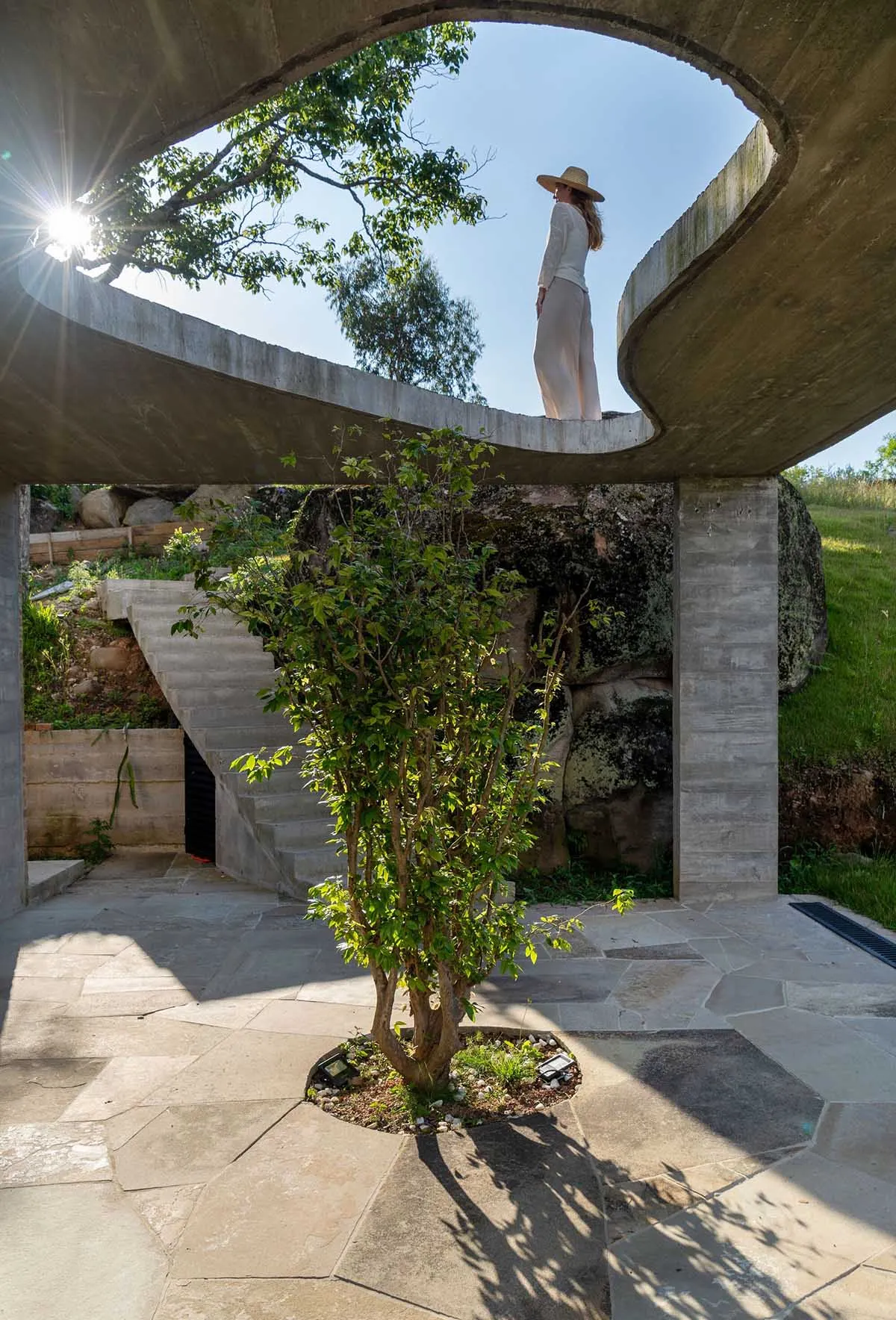 A minimalist outdoor space featuring a concrete archway, stairs, and a tree in a circular patio.