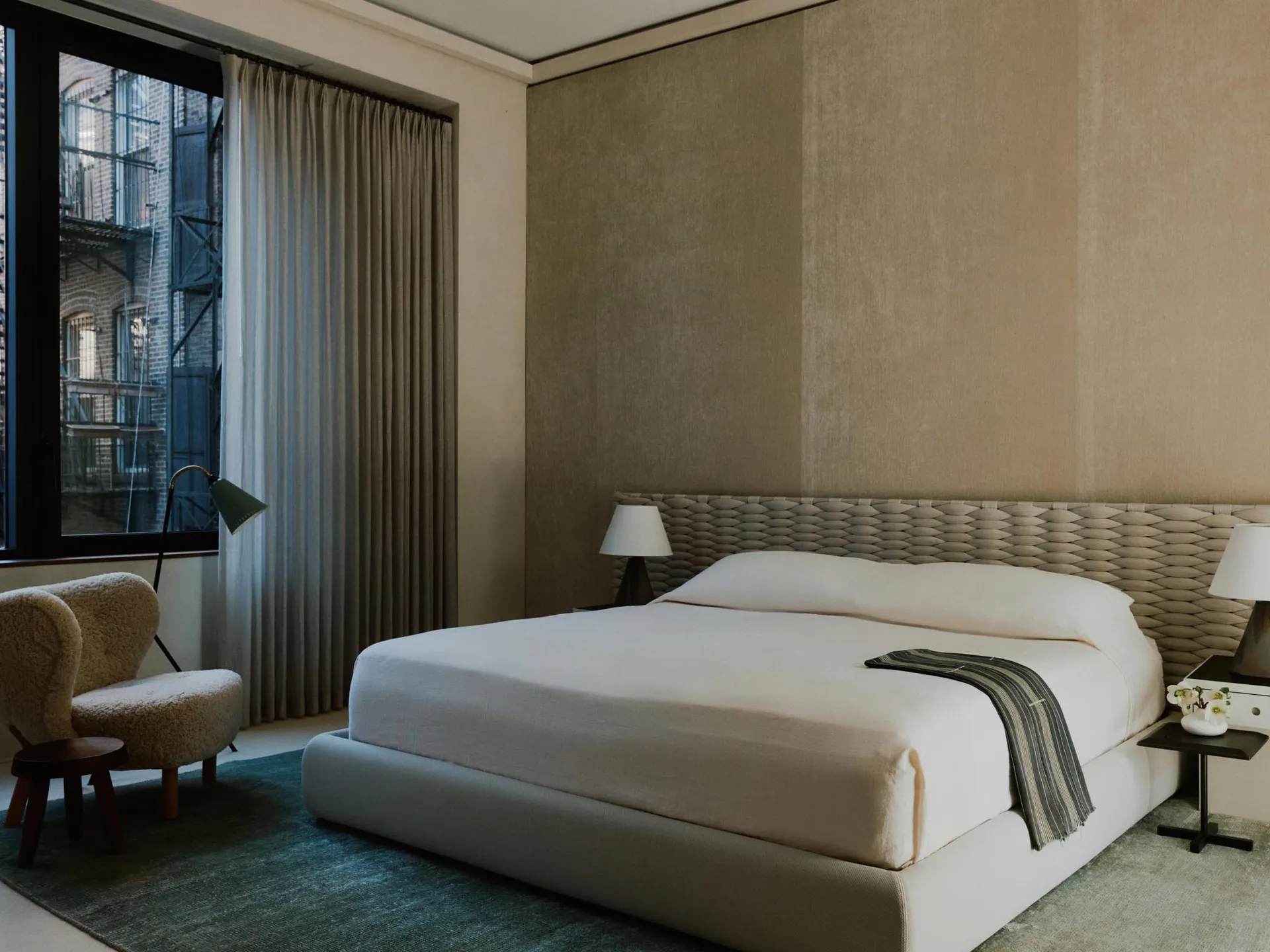 A minimalist bedroom featuring neutral textiles and a textured, woven headboard