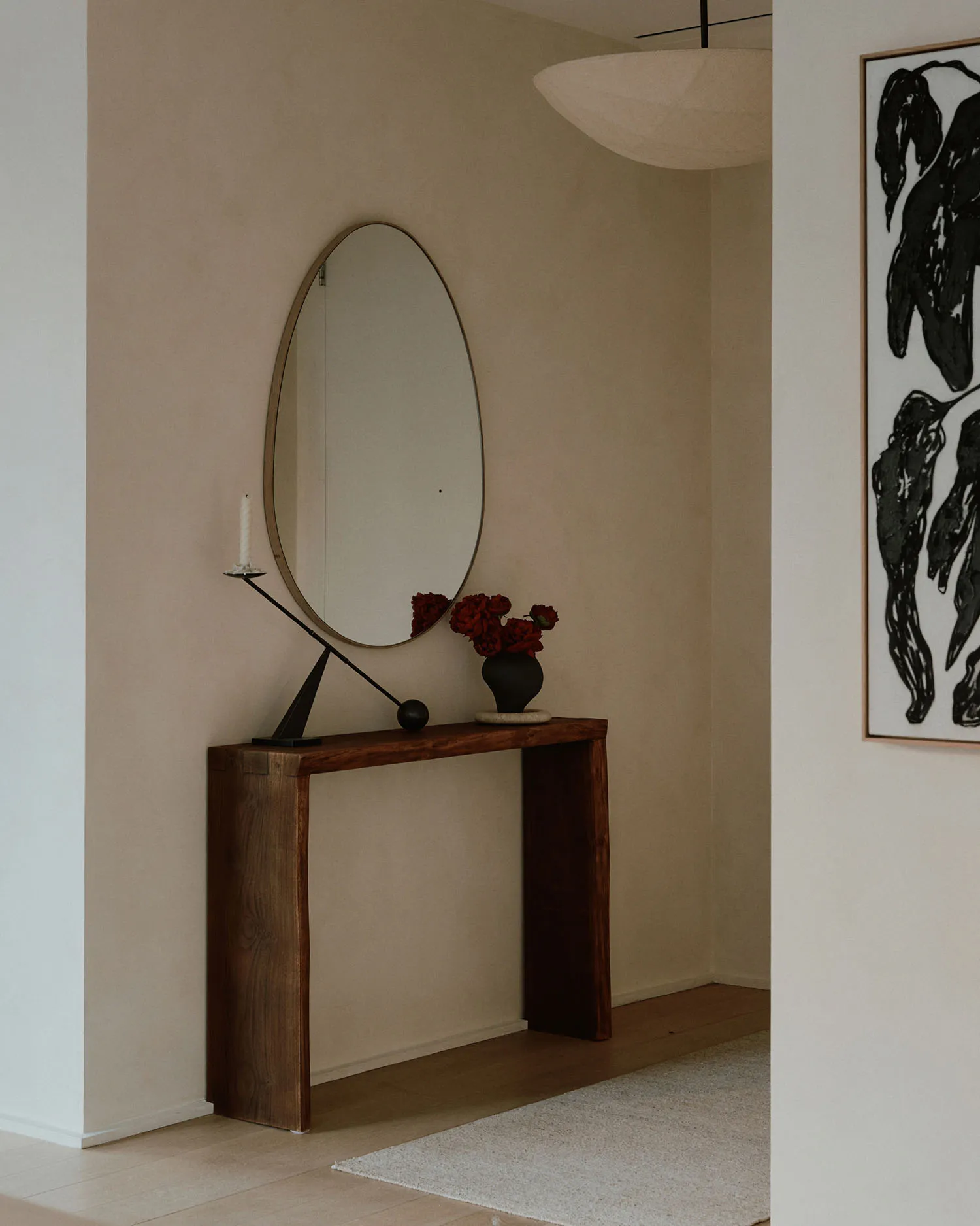 A minimalist entrance console table with a round mirror, red flowers, and a candle holder.