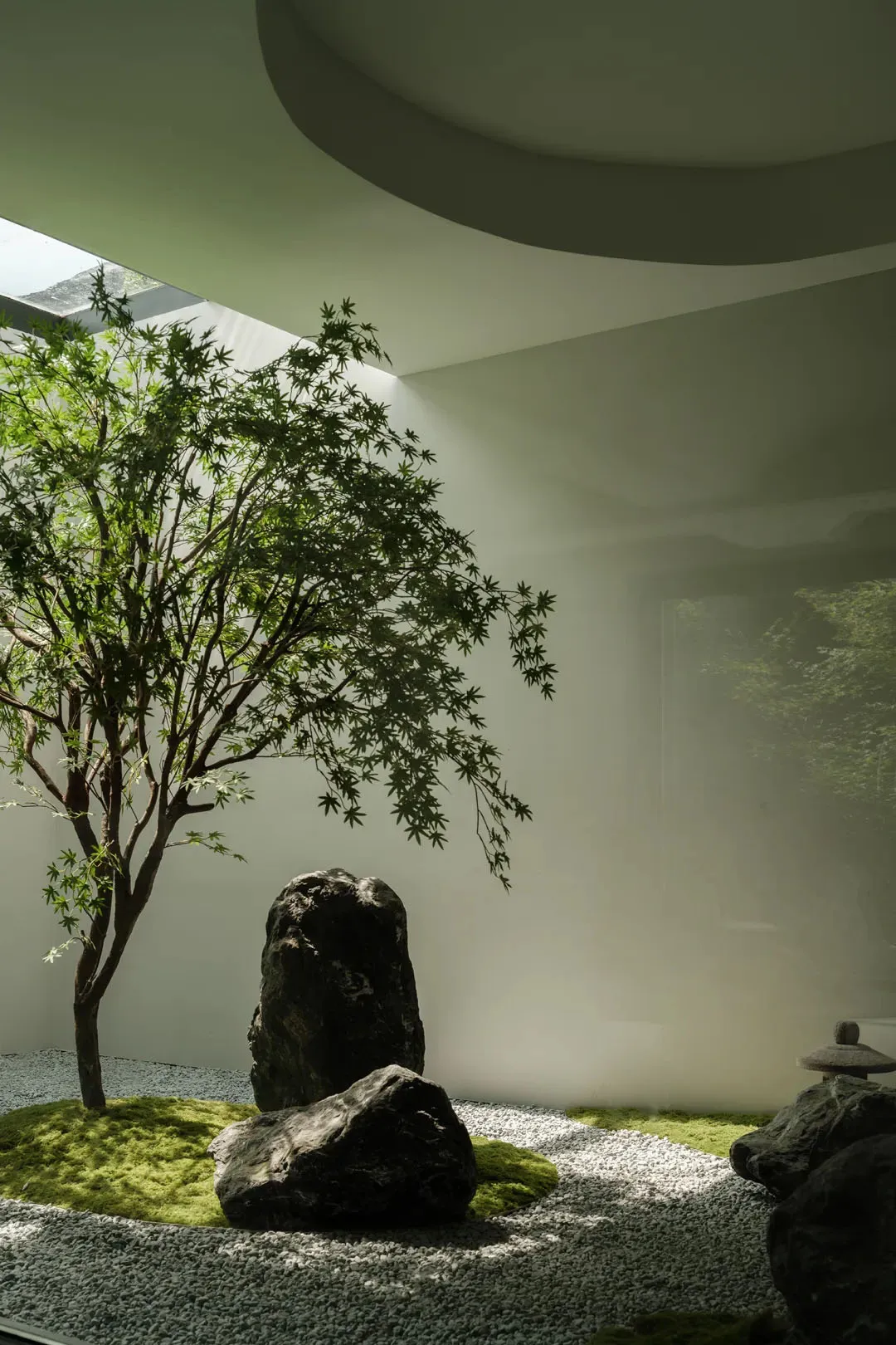 A minimalist indoor garden featuring natural stone and greenery under a circular skylight.