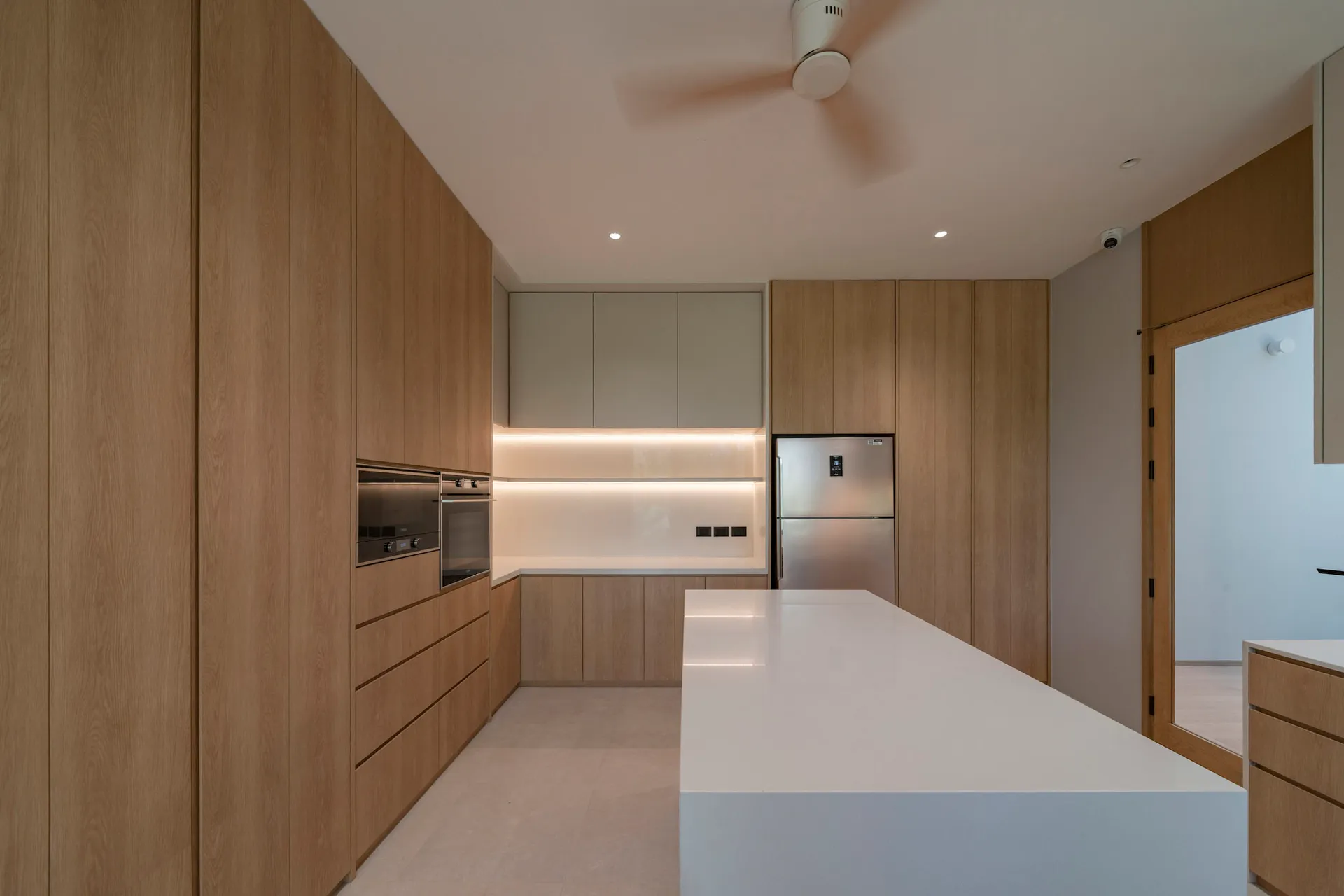 Modern minimalist kitchen featuring wooden cabinets, white countertops, and integrated appliances.