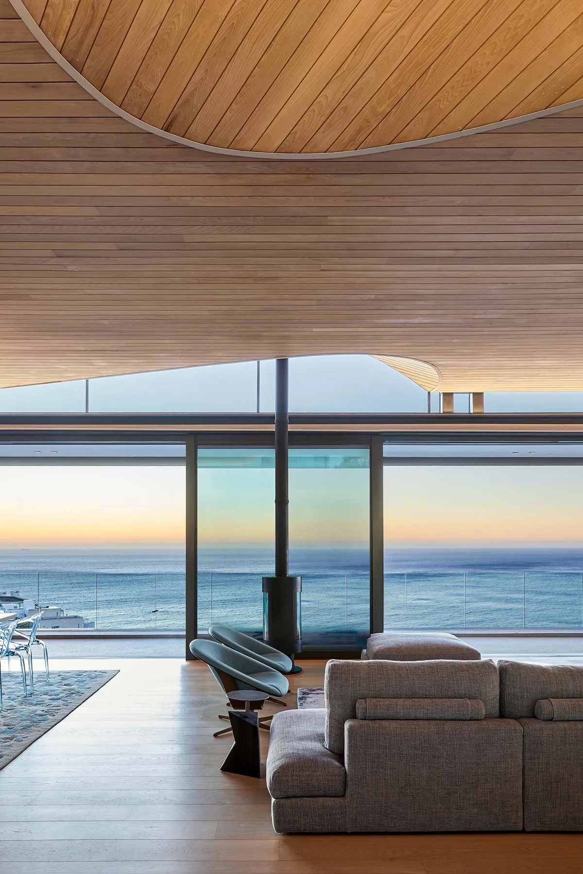 Modern minimalist living room with wood furniture and floor-to-ceiling windows overlooking the ocean.