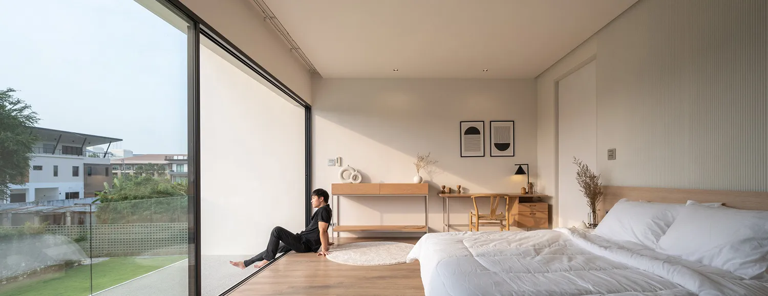 Modern minimalist bedroom with glass wall, wooden floor, and white furniture.