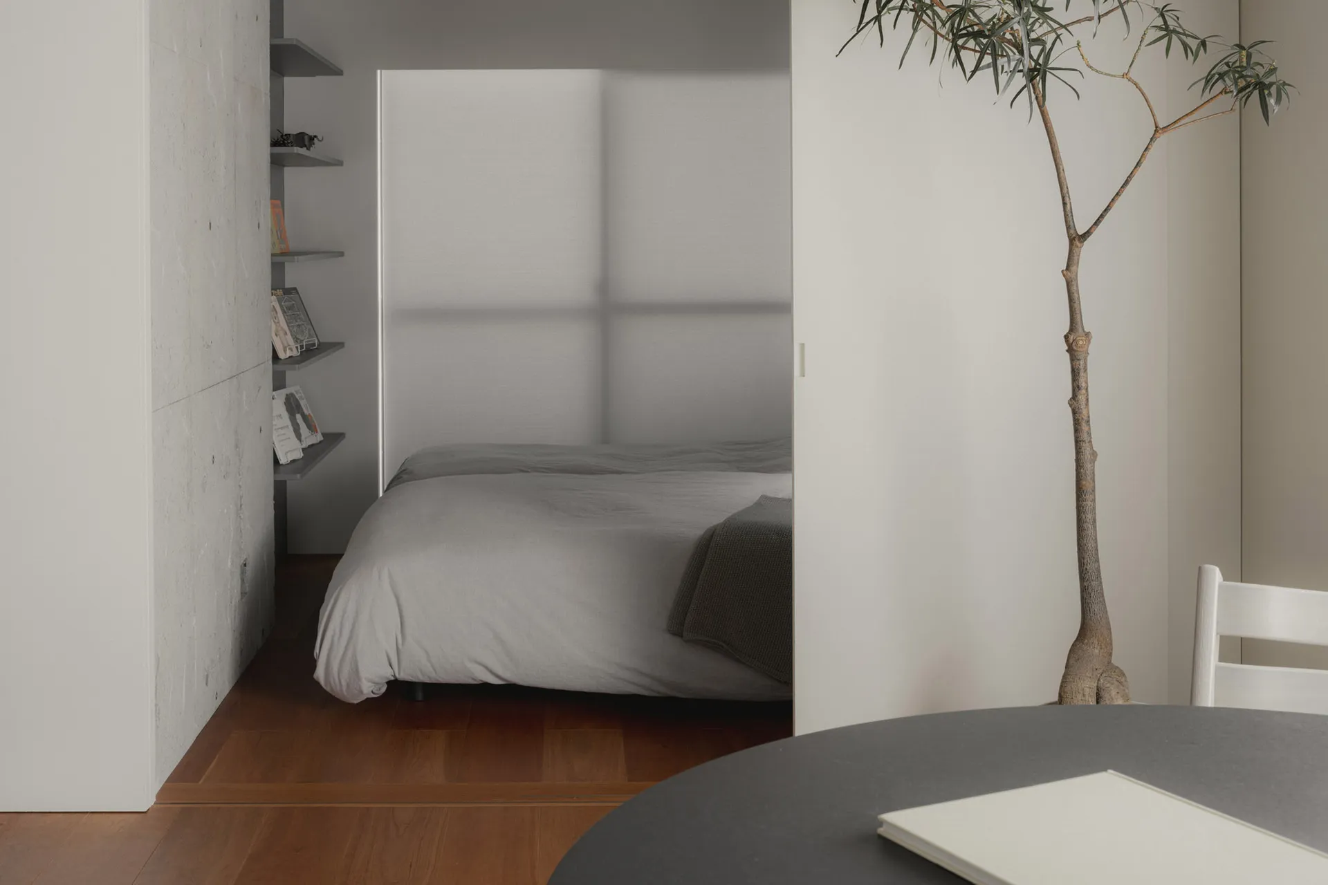 A minimalist bedroom featuring a bed with light-colored sheets on a wood floor.