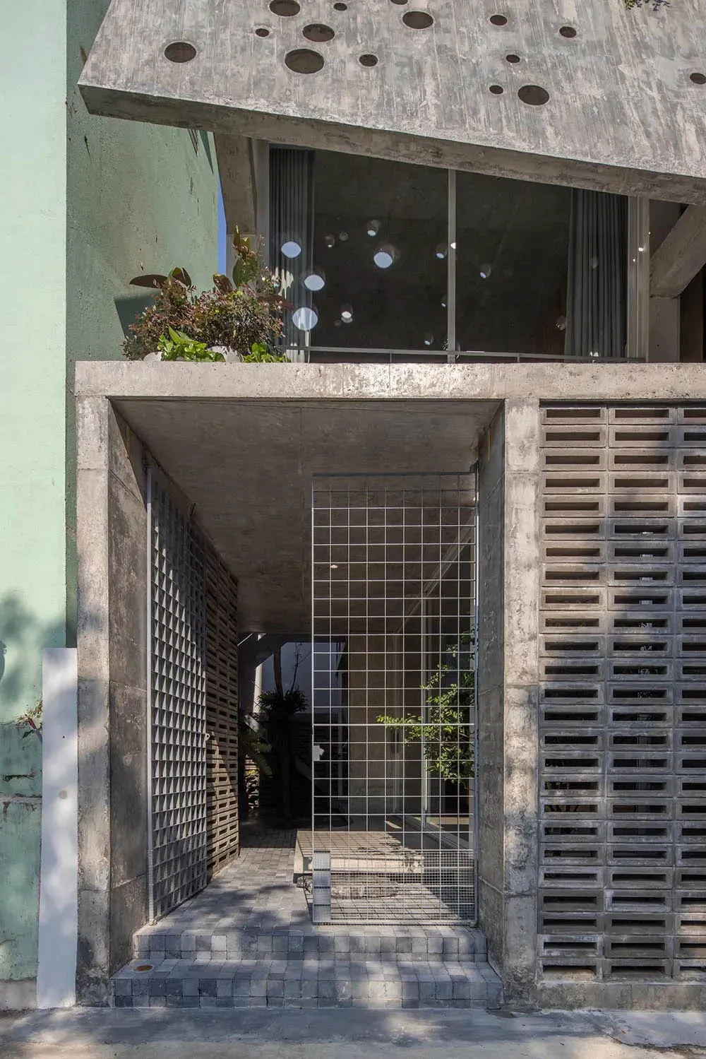 A modern entrance with a concrete facade featuring a grid and lattice design, with a green wall and plants above.