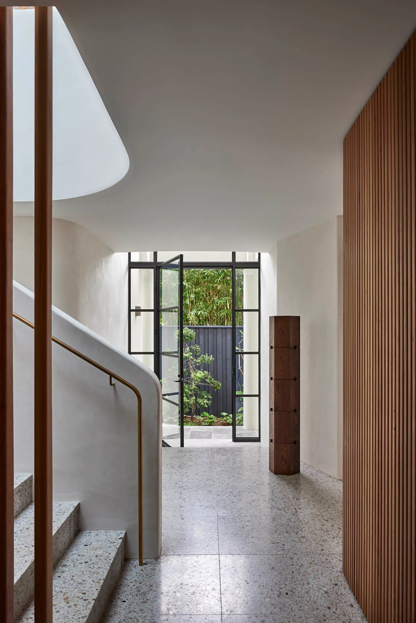 Modern minimalist entrance hall featuring a concrete staircase, glass door, wood accents, and a view of green foliage outside