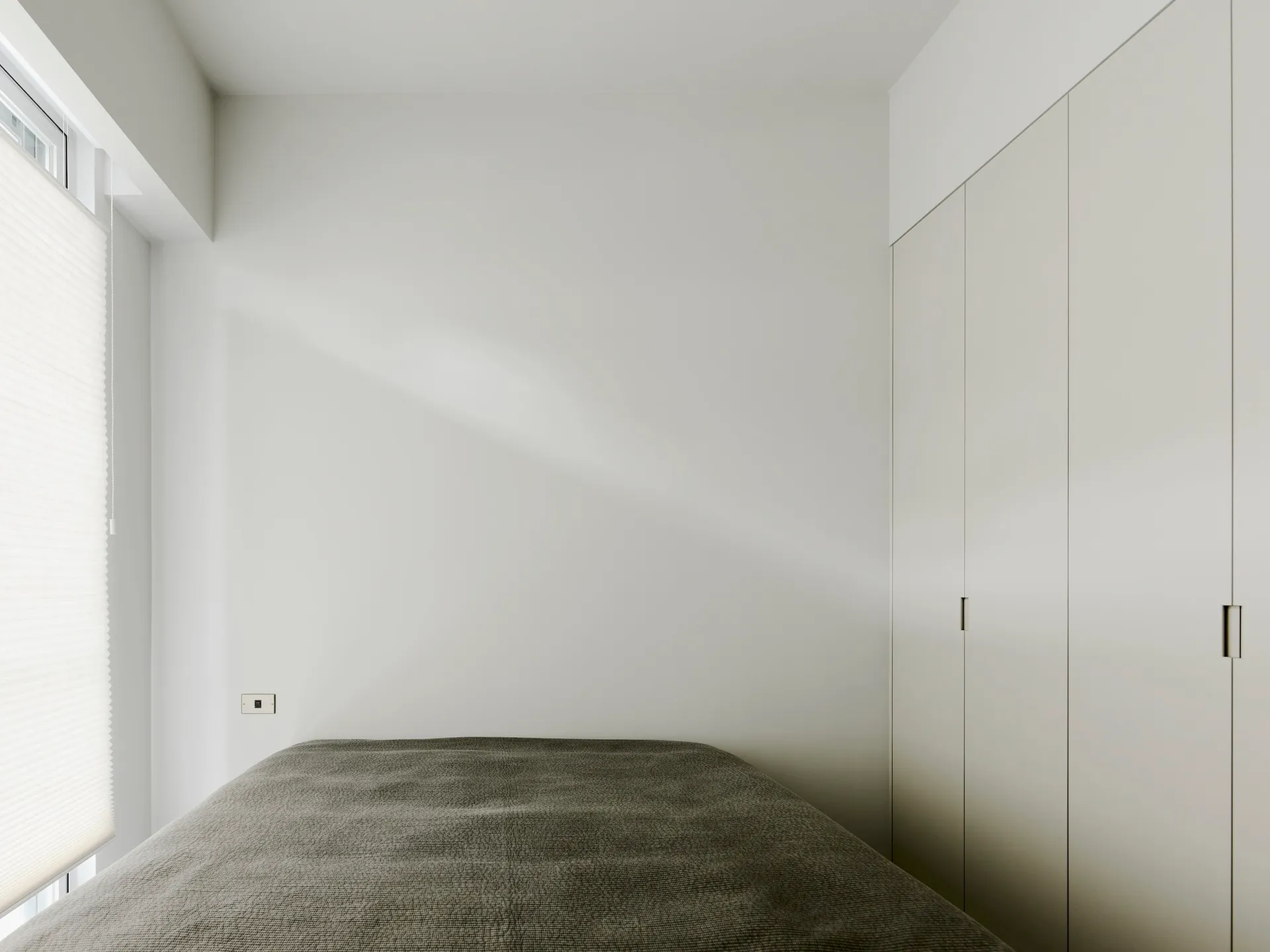 A minimalist bedroom features a soft fabric-covered bed against a white wall.