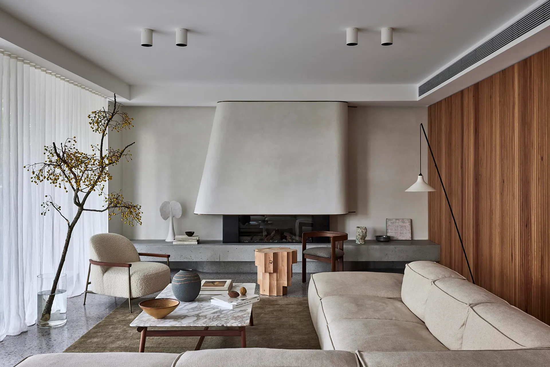 A minimalist living room with a concrete fireplace, wooden walls, and a beige sectional sofa.