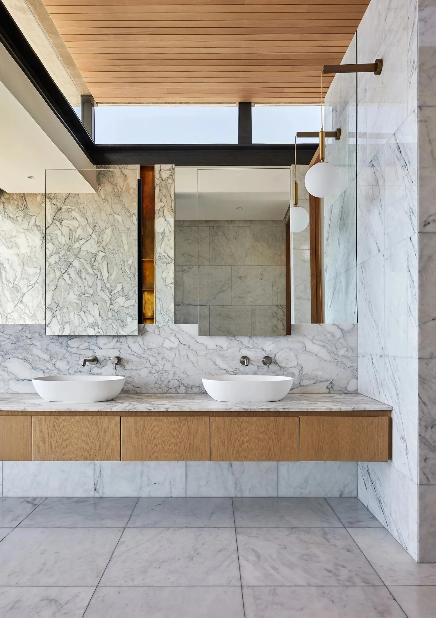 A modern minimalist bathroom featuring a white marble countertop with two sinks, wooden cabinetry, a large mirror, and a larg