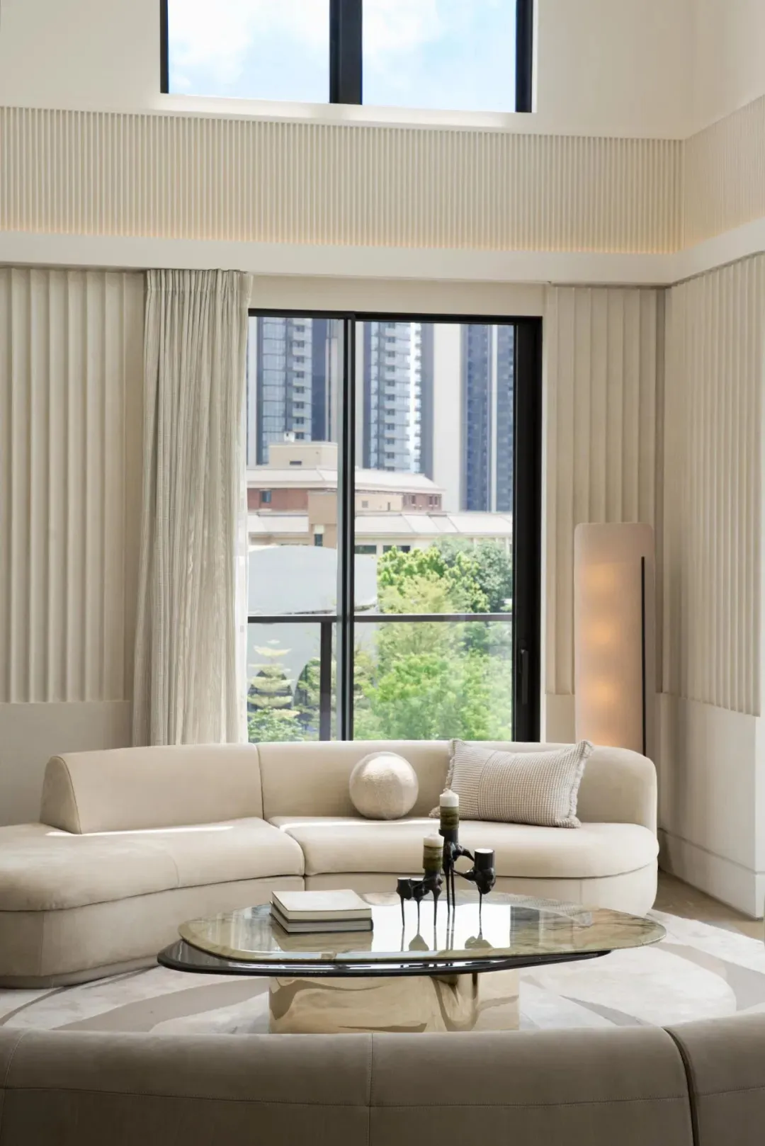 A minimalist living room featuring neutral-colored furniture and a large window with city views.