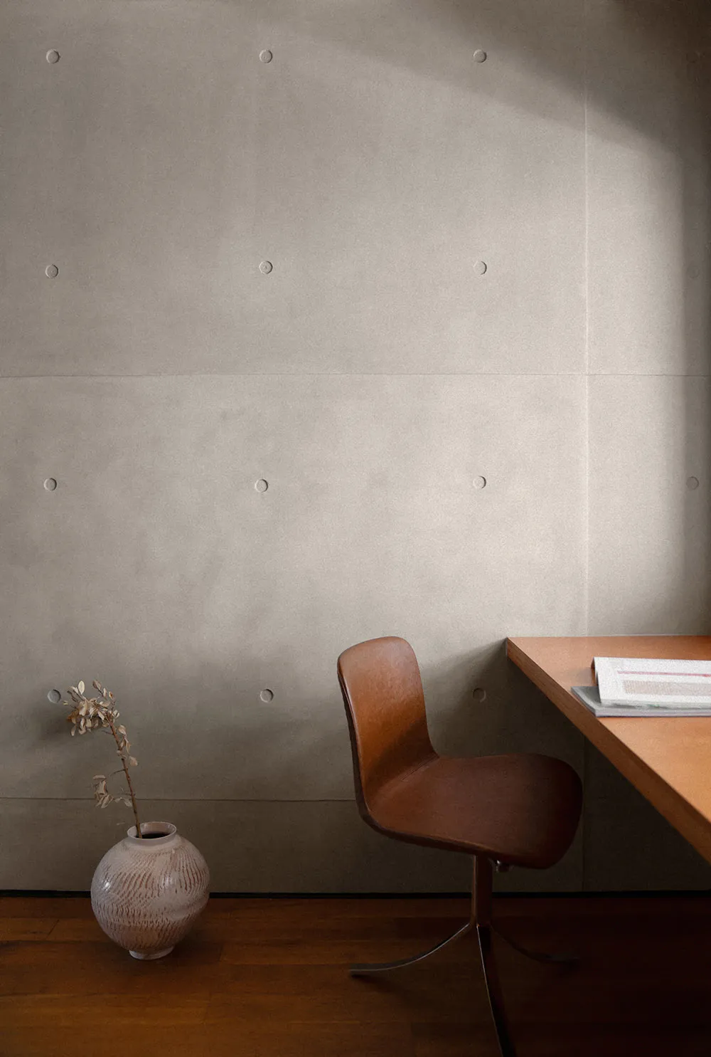 A minimalist workspace featuring a wooden frame and desk, with a brown chair and a small vase with a plant.