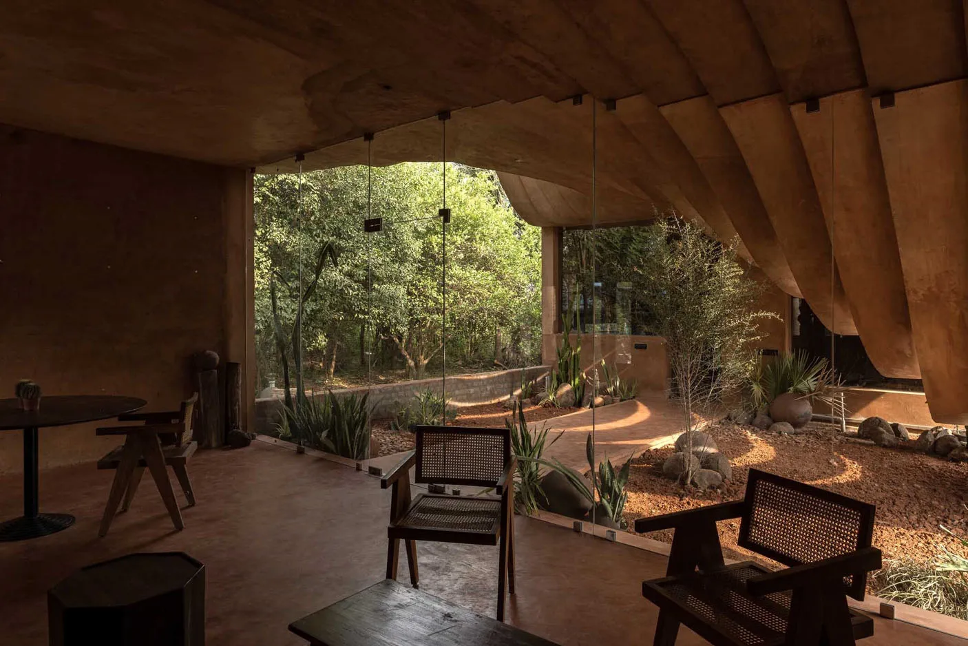 A modern living room with exposed concrete walls and ceiling, featuring large windows with a view of a lush green garden.