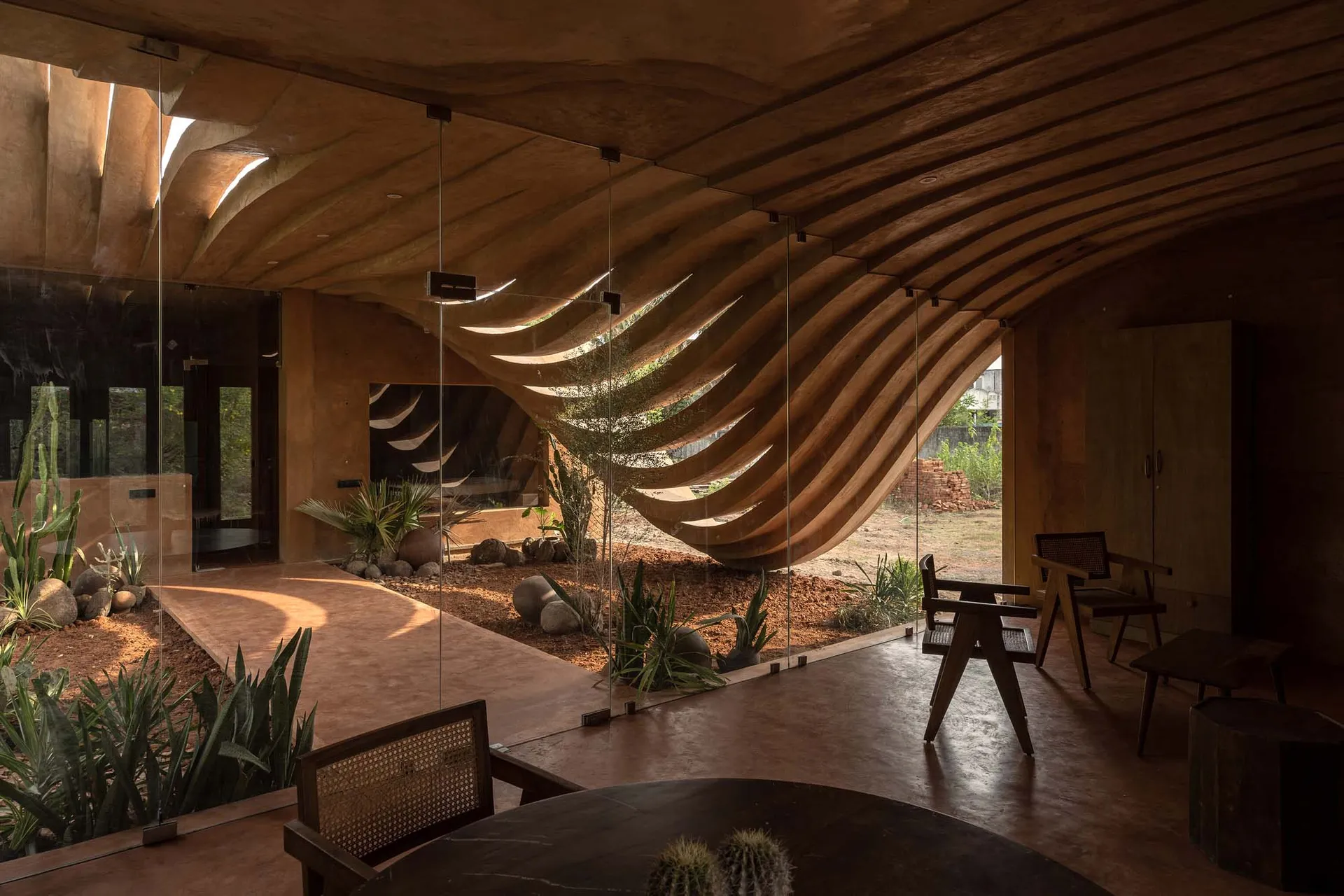 Modern industrial living room with concrete walls, floor, and ceiling beams, featuring natural light and greenery.