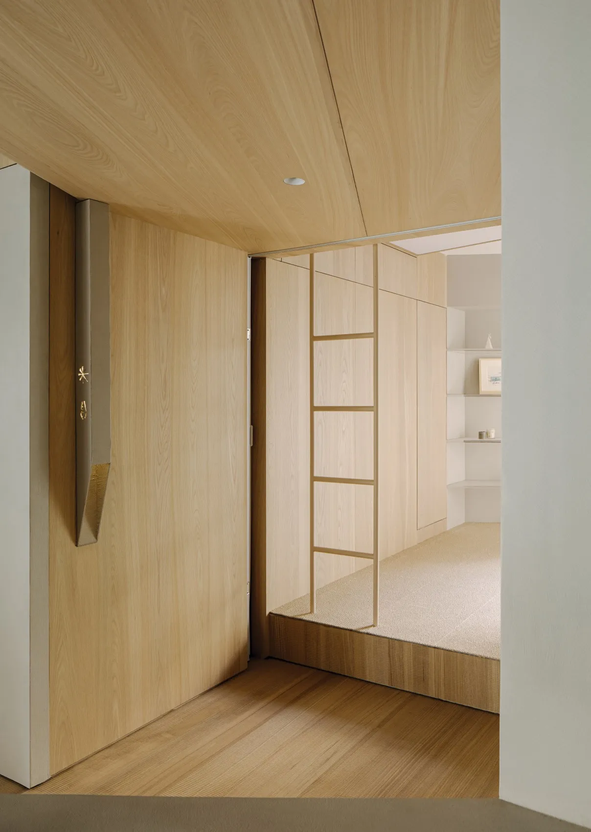 A modern minimalist bedroom with light wood walls and floor, featuring a ladder-like structure leading to a raised sleeping a