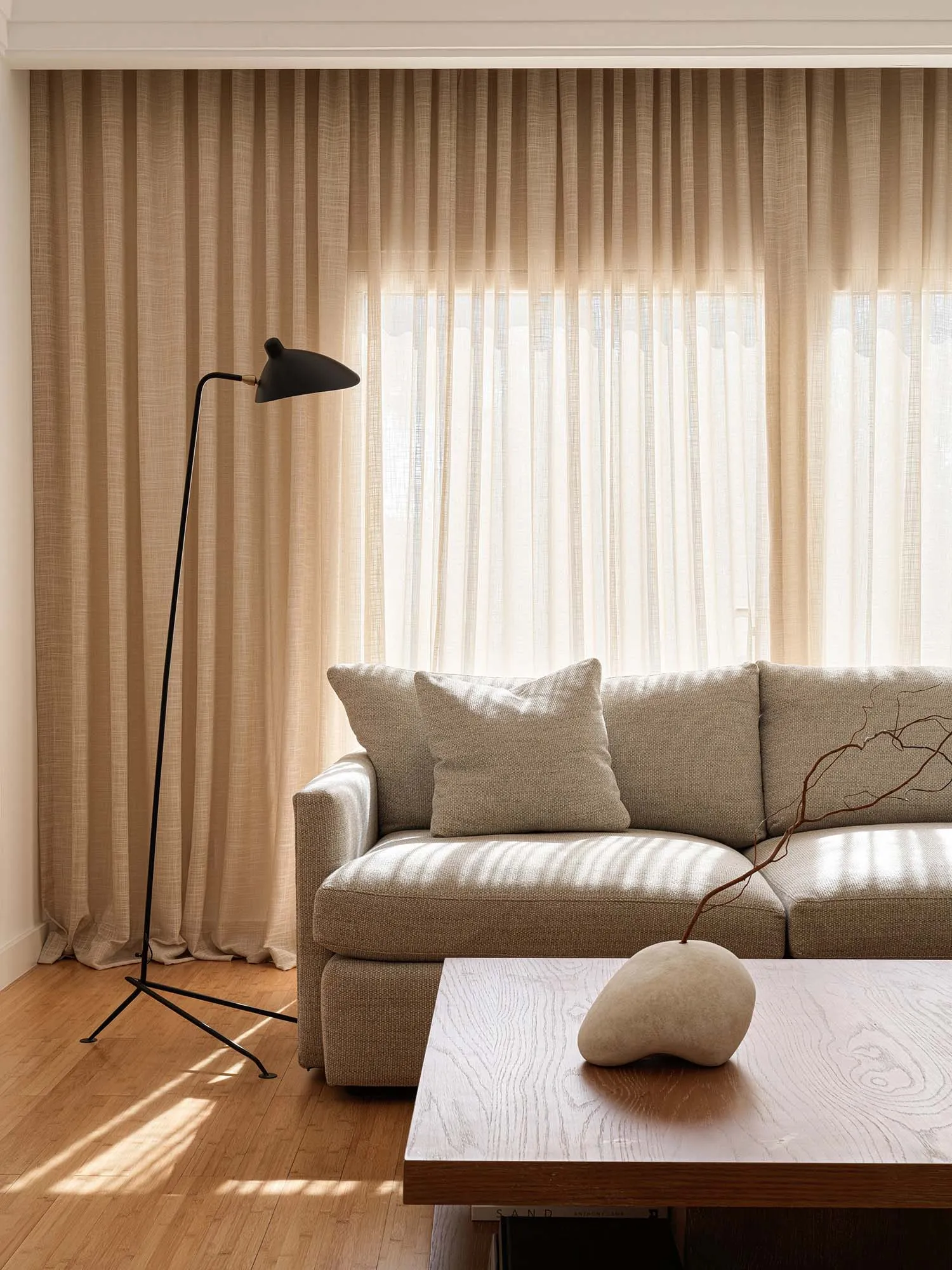 A modern, minimalist living room featuring a sleek fabric couch, wooden coffee table, and floor lamp with a black tripod base