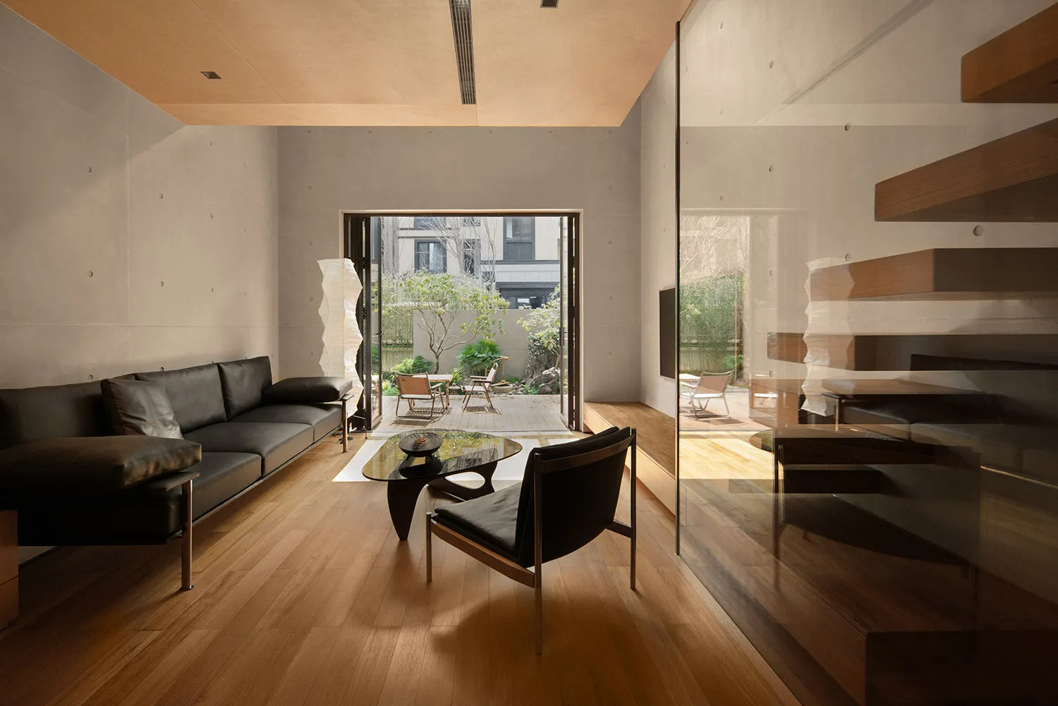 Modern minimalist living room with black and brown furniture, wooden floors, and a glass coffee table.