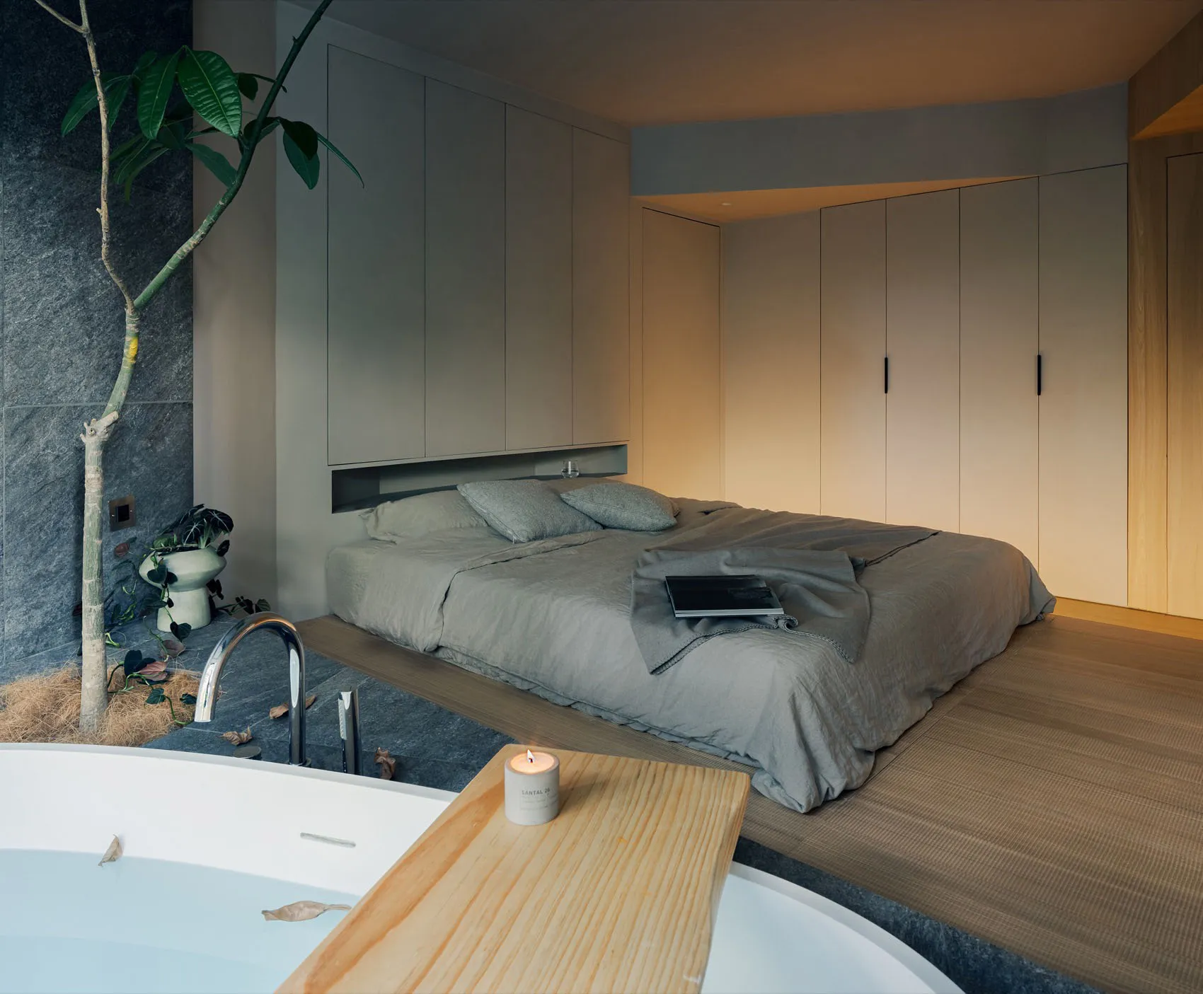 A minimalist, modern bedroom with a bed on a wooden platform, grey bedding, and a built-in wardrobe.