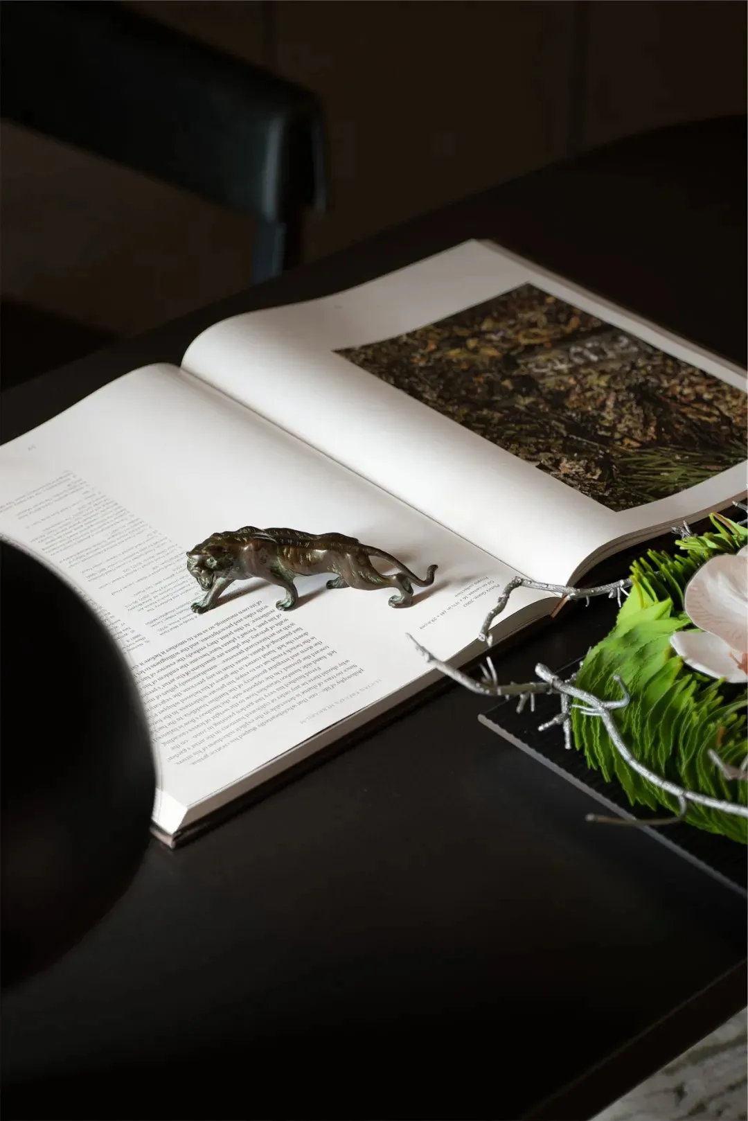 A metal sculpture of a cat on an open book with greenery and a flower arrangement.
