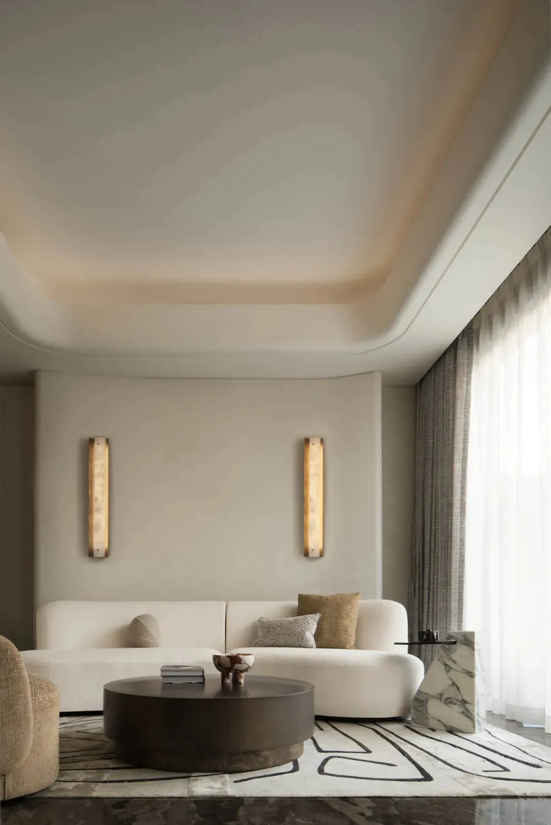 A minimalistic living room with a white sofa, marble coffee table, and textured fabric accents.