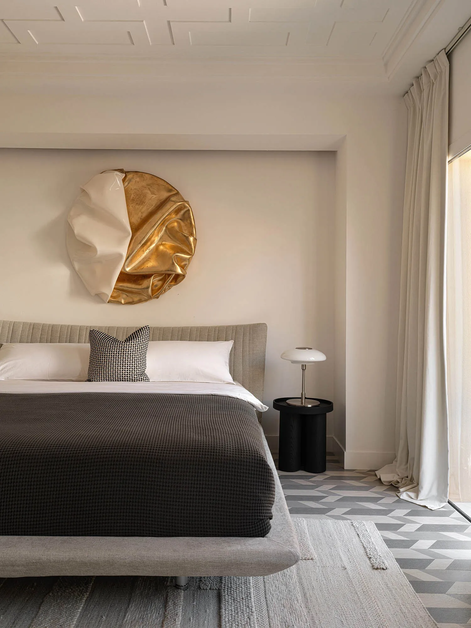 A modern bedroom featuring a neutral color palette, a textured bedspread, and an artistic circular ornament hanging above the