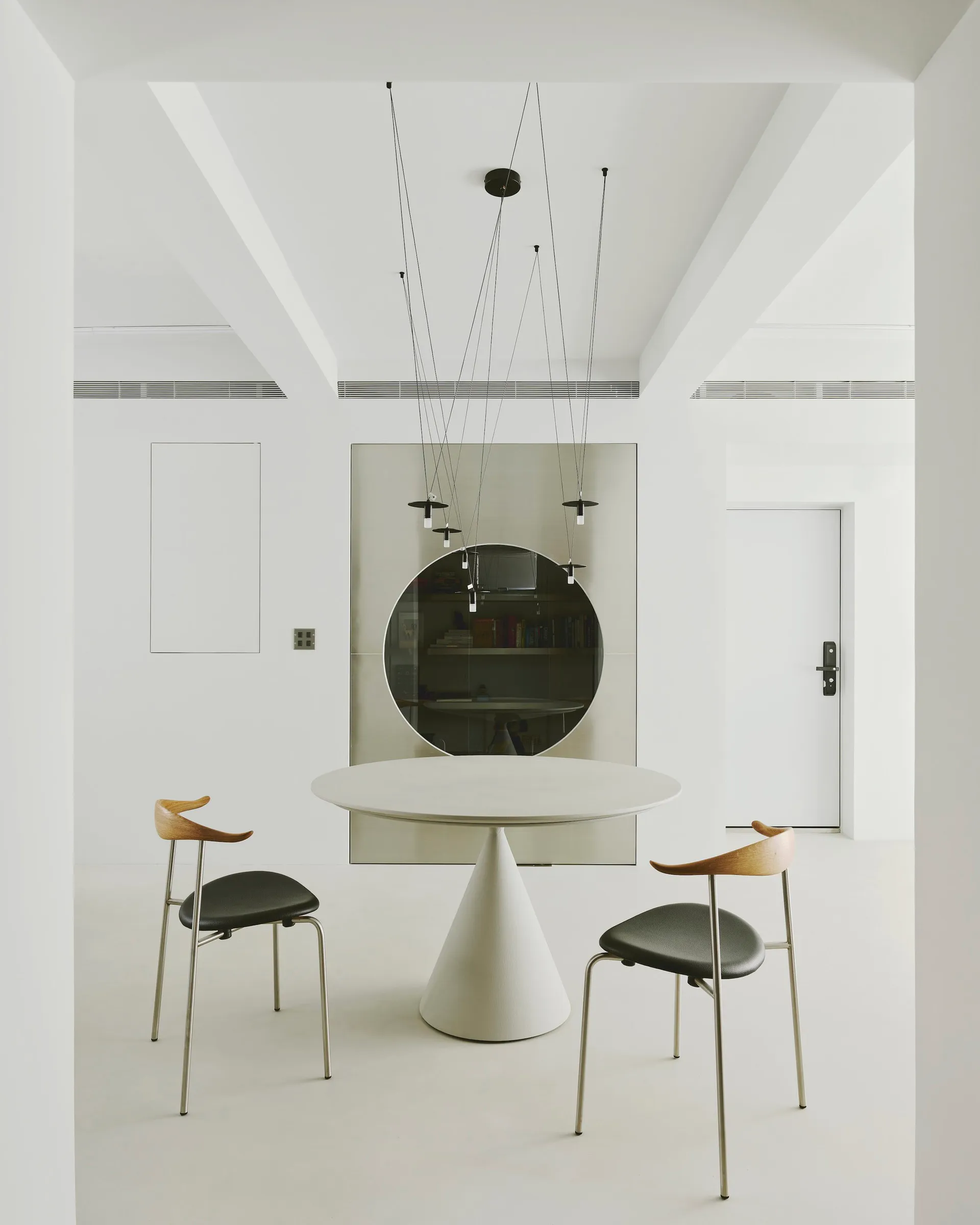 A modern dining room featuring a round table with a cone-shaped base and two chairs with black seats and wooden backs.
