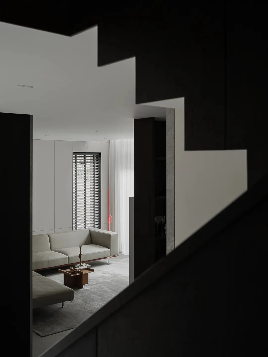 Contemporary modern minimalist living room with white furniture and dark staircase.