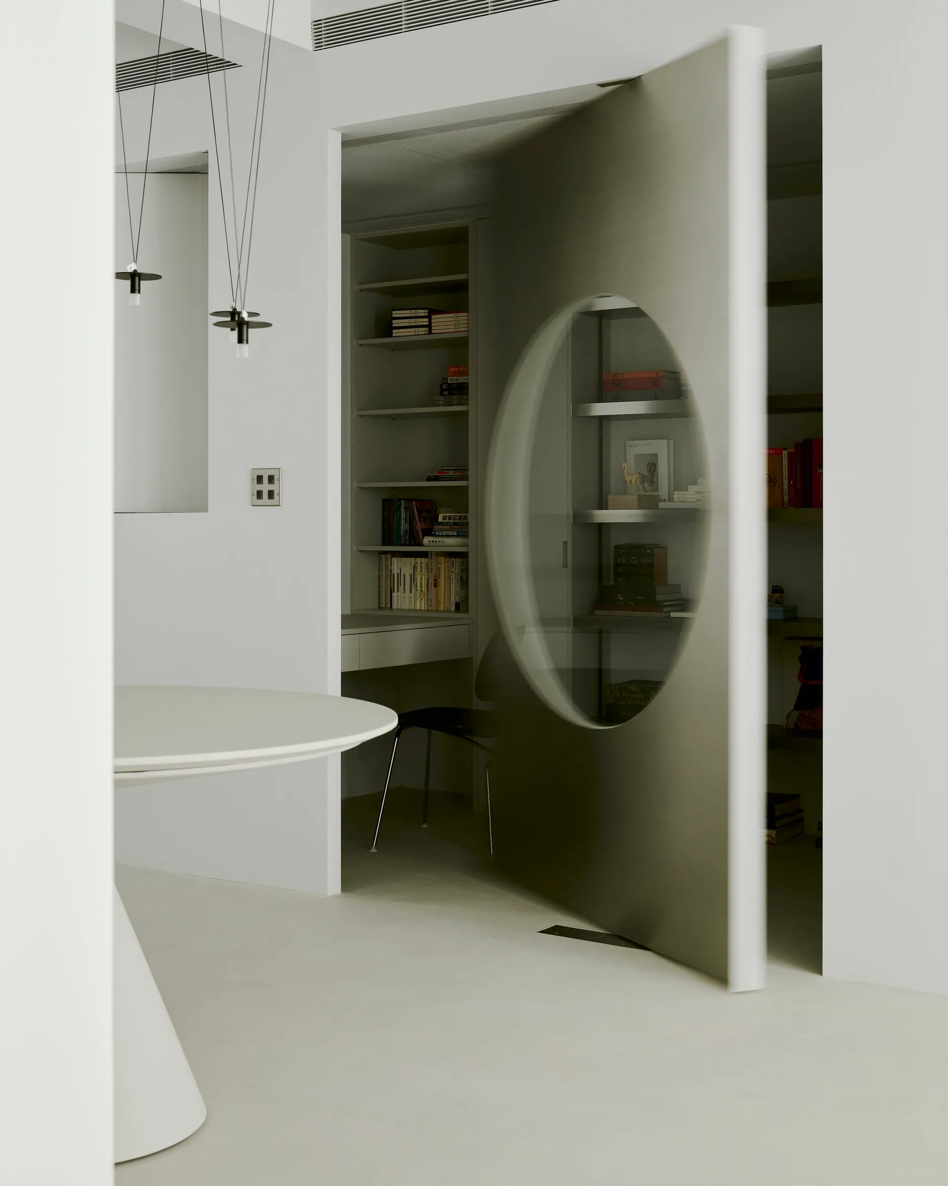 Modern minimalist library with concrete walls and floor, featuring a circular cutout in the wall, shelves filled with books a