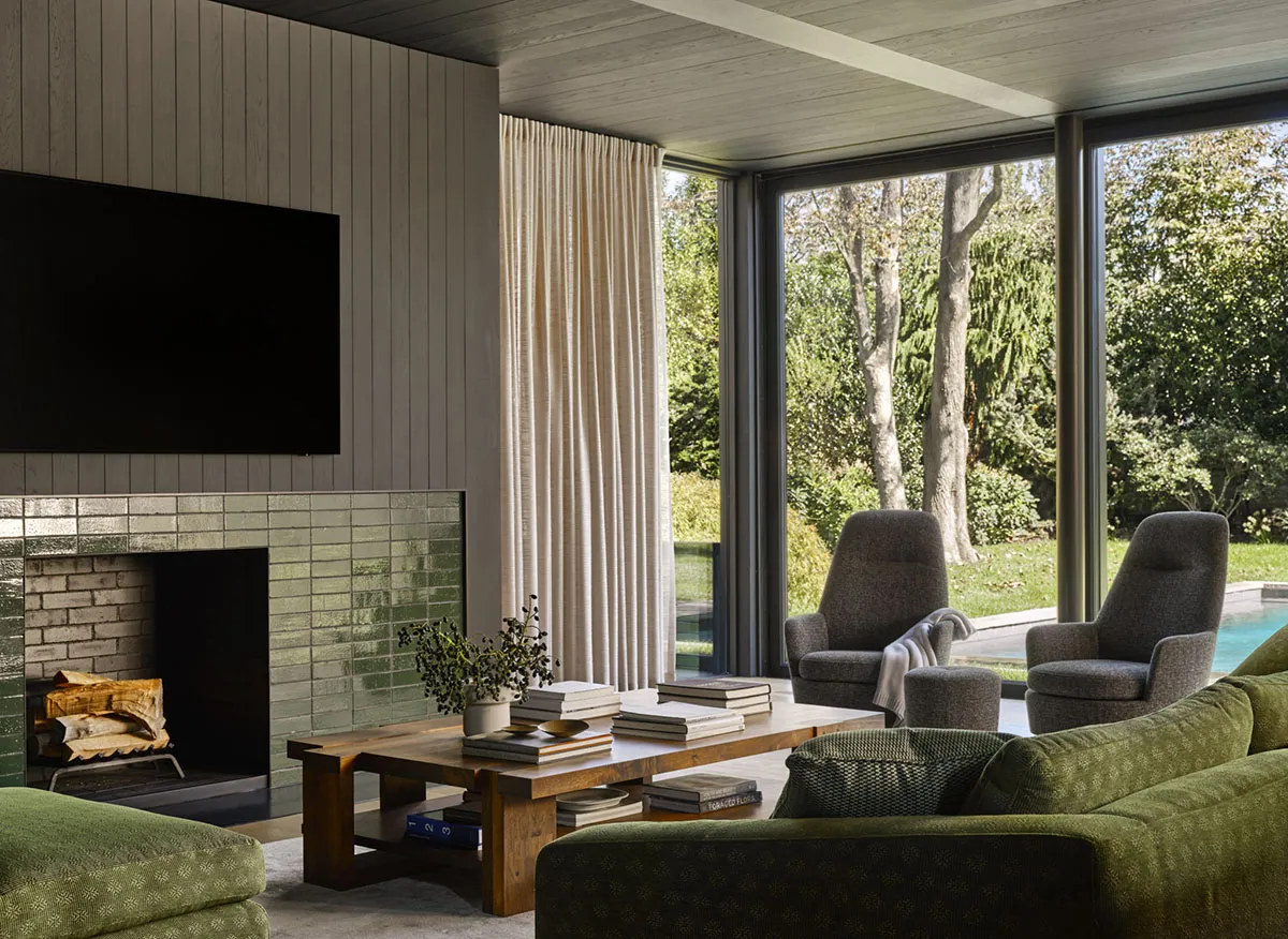 A contemporary living room featuring a tile fireplace and large windows overlooking a garden.
