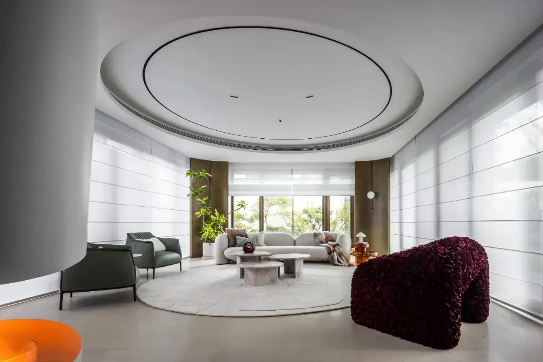 A minimalist living room with a white circular ceiling, modern furniture, and large windows.