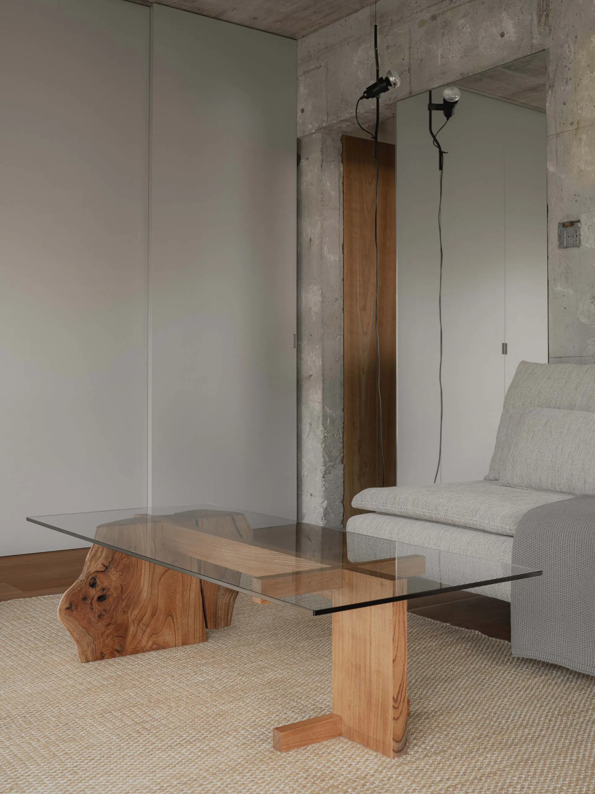 Modern industrial interior living room with glass table, wooden elements, and concrete walls.
