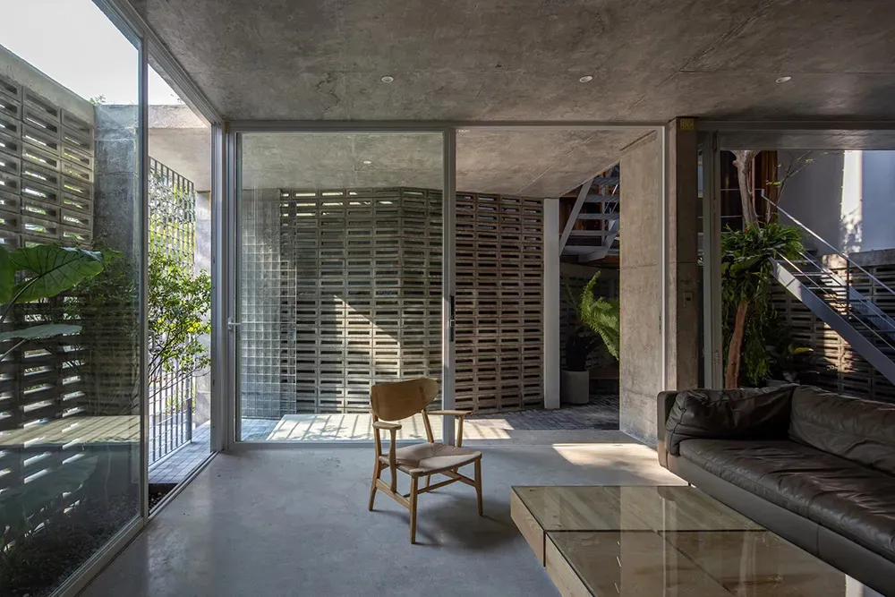 A minimalist living room with a concrete floor and walls, featuring a wooden armchair, a leather sofa, a glass coffee table,