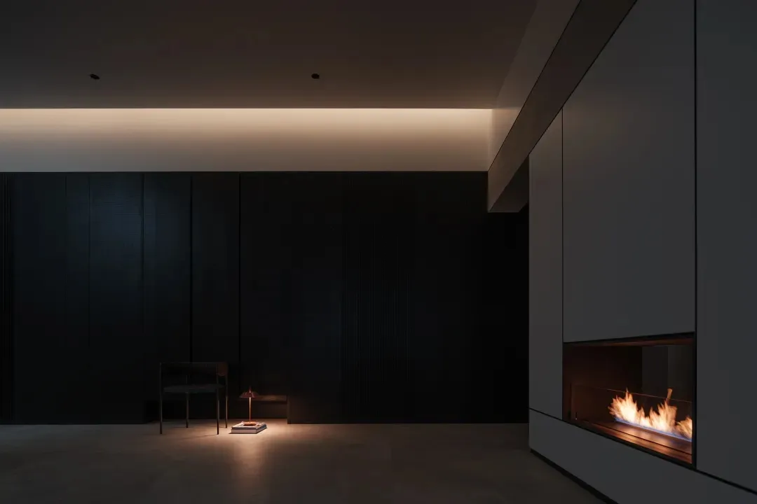 A minimalist living room featuring a concrete floor and walls, with a cozy fireplace and a solitary chair.