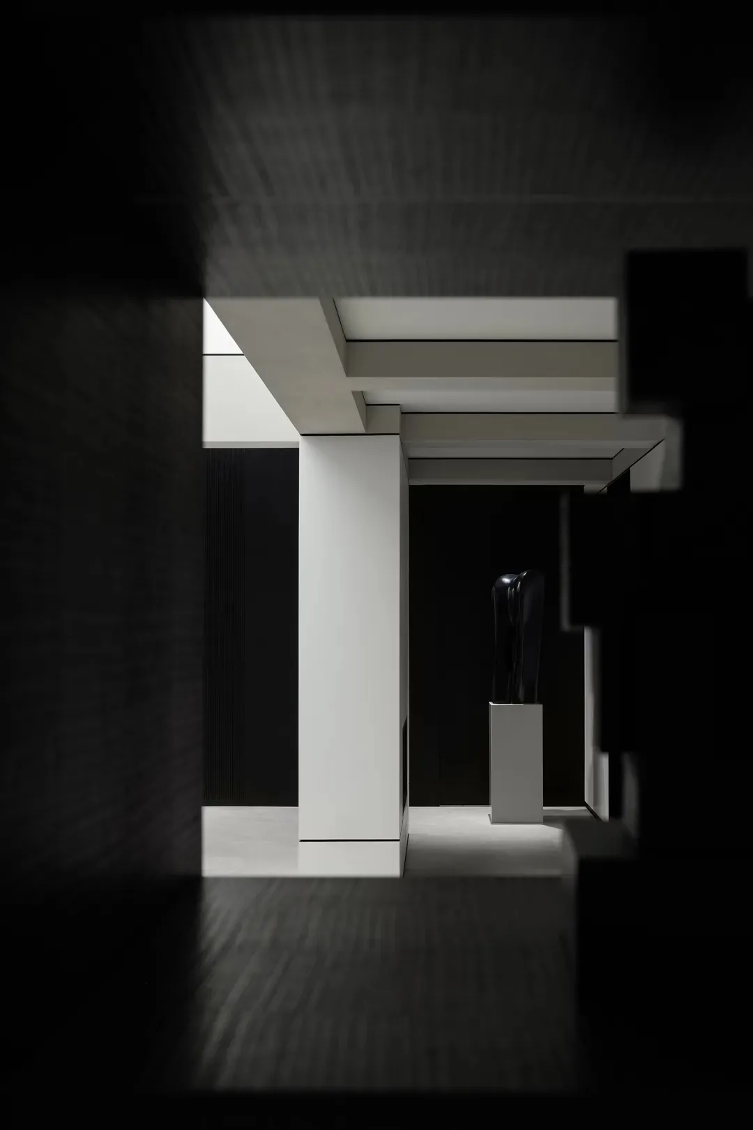 A minimalist interior with black and white elements, featuring concrete walls and a black sculpture.