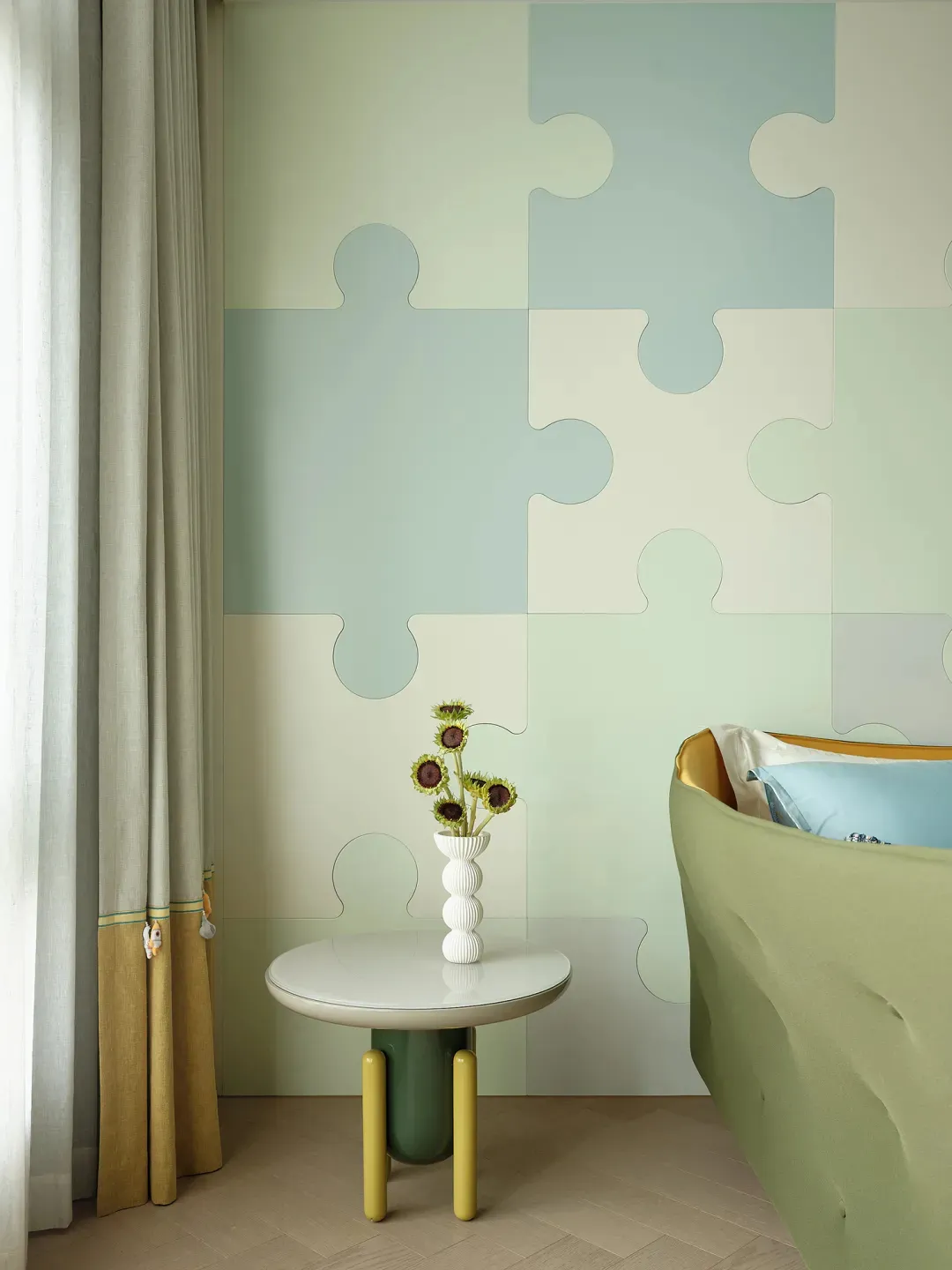 A bedroom featuring a wall covered with fabric panels, a green round table with a vase of sunflowers, and a blue and yellow b