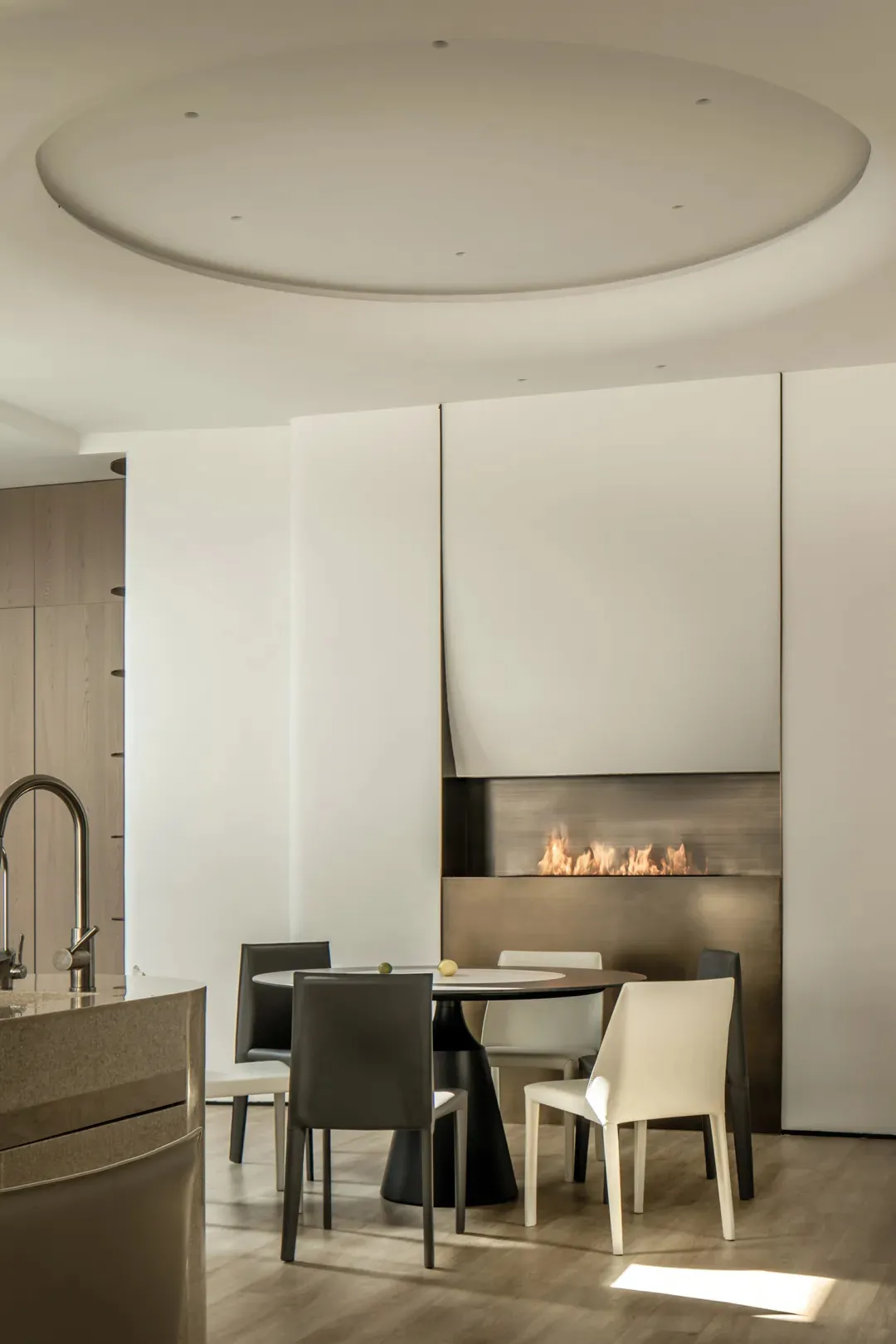Modern dining room featuring a circular metallic table with white cushioned chairs and a minimalist fireplace.