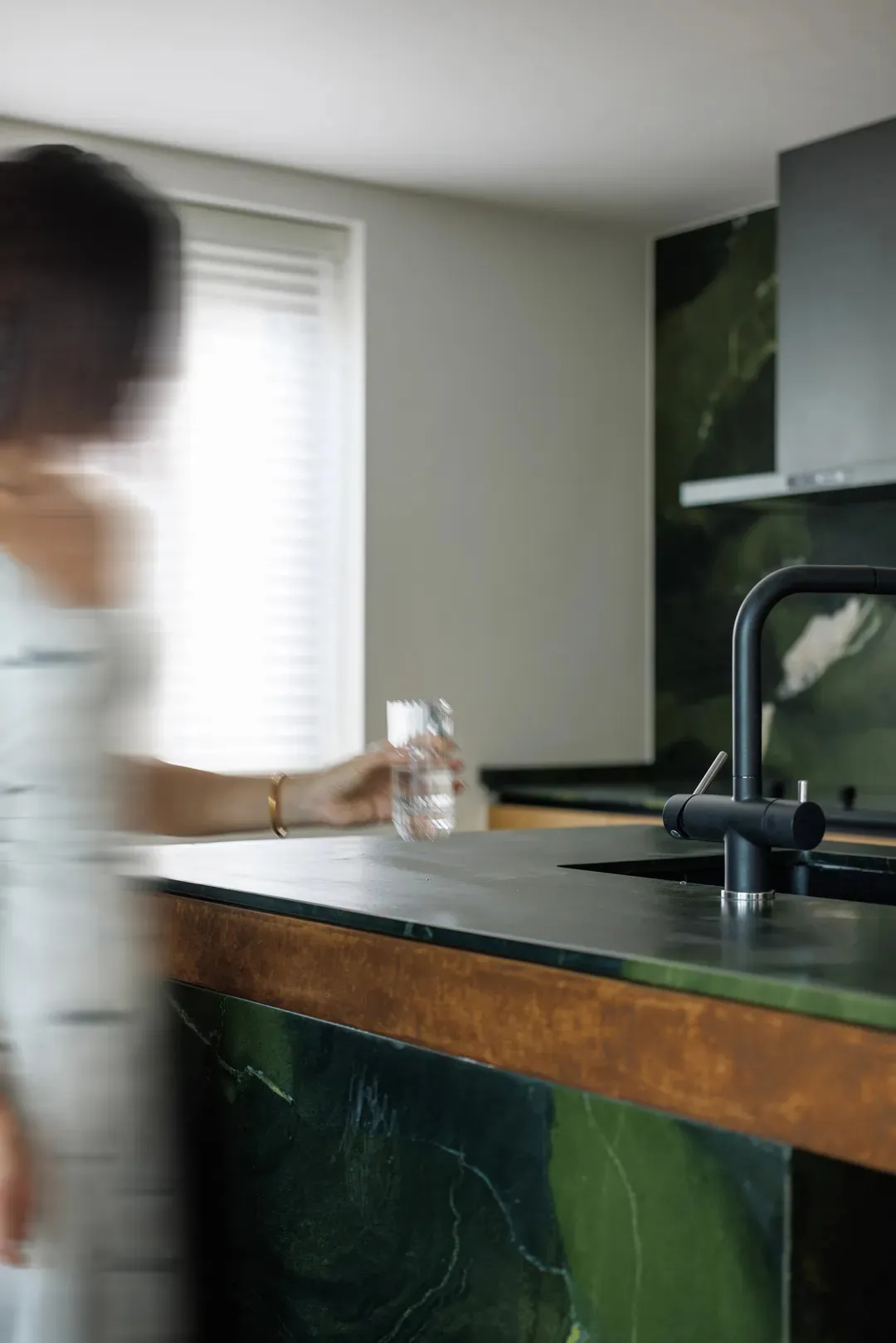 A modern kitchen with green marble countertops and a black faucet.