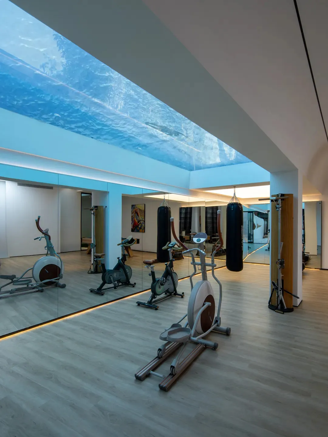A modern gym featuring glass walls and a water floor, with various exercise equipment.