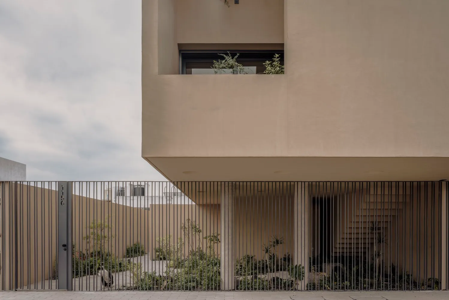 A modern house with a concrete exterior featuring a large patio and a metal fence.
